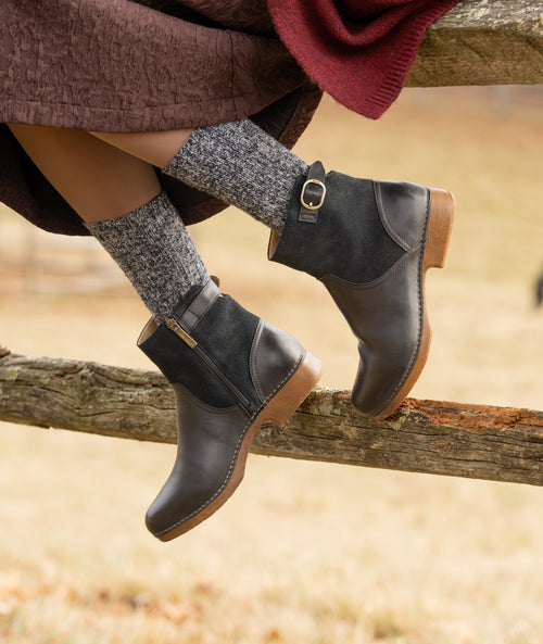 Woman sitting on a fence wearing Dansko Monique Boots in Black
