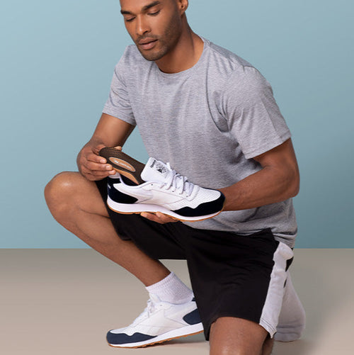 Man kneeling putting an Aetrex insole into his shoe