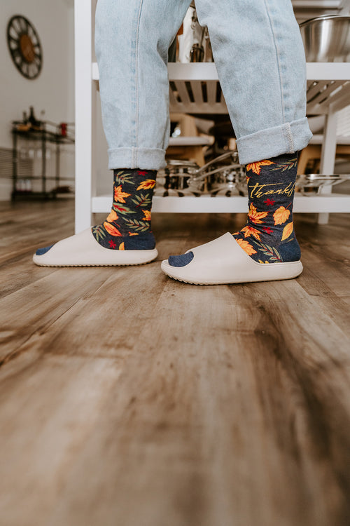 Woman standing in the kitchen wearing Thankful For Fall Socksmith socks and white slides